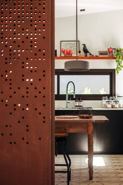 La puerta corrediza de acero Corten con pátina incolora vincula el living-comedor con la cocina.