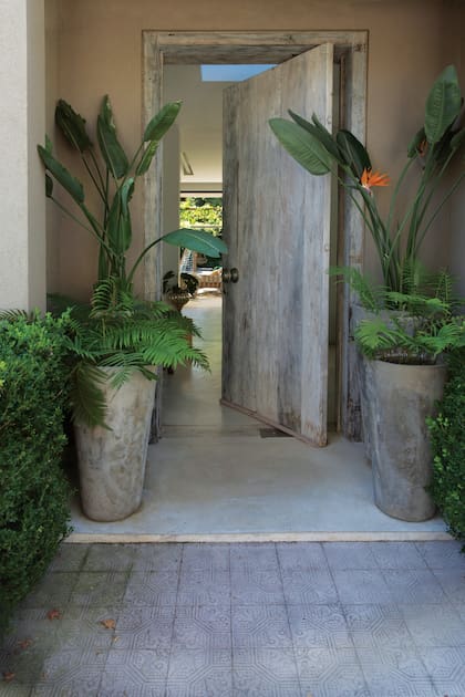 La puerta de entrada, de madera, escoltada por dos maceteros circulares de cemento.
