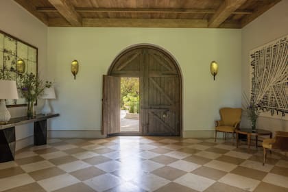 La puerta de entrada es una de las grandes protagonistas de esta casa. “Me recordó a las iglesias de Milán, tienen puertas así de majestuosas, pero que, para entrar tenés que bajar la cabeza”, cuenta Nunzia. Los sillones son de anticuarios y fueron retapizados. La obra de la derecha es de Pablo Siquier; y los pisos en damero, de piedra