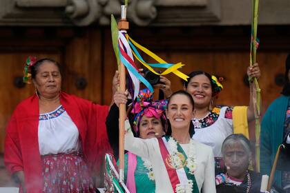 La recién investida presidenta de México, Claudia Sheinbaum, sonríe mientras sostiene el bastón de mando durante una marcha en el Zócalo.