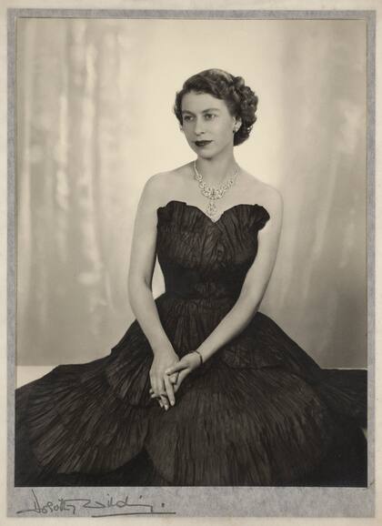 La reina Isabel, veinte días después de su ascensión al trono. La Oficina de Correos y la Royal Mint concedieron la primera sesión oficial de la monarca a Dorothy Wilding. El vestido de noche de tafetán negro, la pose y la elección de joyas se consideraron inadecuados para las necesidades de los comisionados, por lo que se tuvo que hacer una nueva producción.