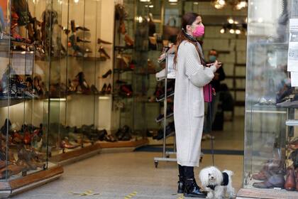 Una mujer con una máscara protectora sostiene a un perro mientras mira una zapatería cerca de la Fontana de Trevi, en Roma
