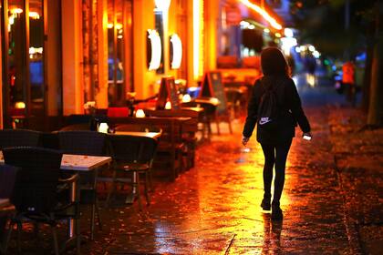 Una mujer camina por una zona de bares con mesas vacías antes del toque de queda nocturno, por la pandemia de coronavirus, en Berlín, Alemania