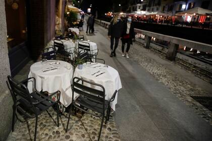 La gente pasa junto a las mesas vacías de un restaurante en el canal Naviglio Grande, uno de los lugares favoritos para la vida nocturna en Milán