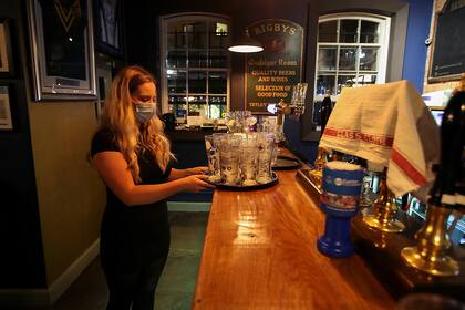 Una empleada lleva una bandeja de vasos vacíos, después de los últimos pedidos en el pub The Bridewell, en Liverpool, Gran Bretaña