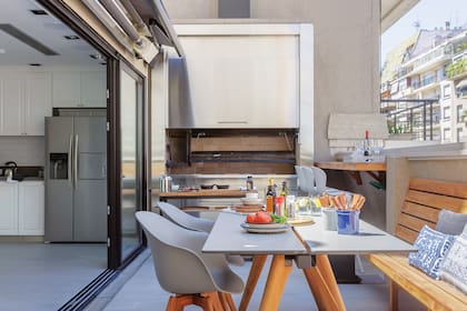 La terraza está equipada con una cocina de apoyo (Carpintería Roldán) en línea con la parrilla con frente de acero inoxidable (Sabato Pagliocca). Aberturas de PVC (Rehau). Pisos de porcelanato (SBG). Juego de mesa y sillas ‘Adelaide’ (BoConcept). Mesa carro ‘Lyon’ (Paul French Gallery).