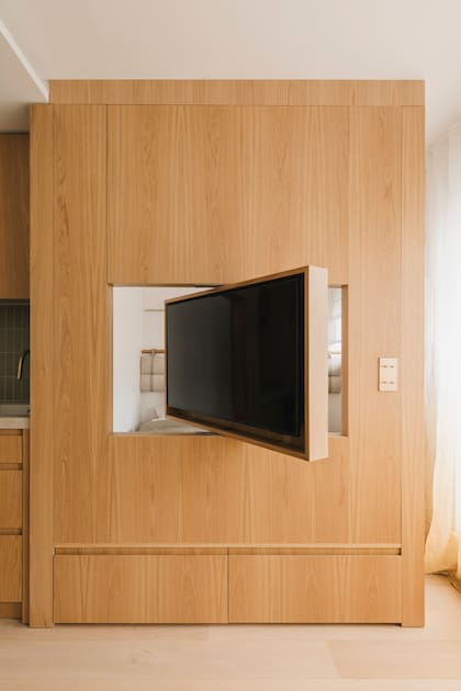 La TV pivotante en movimiento permite vislumbrar la cama detrás del panel de madera.