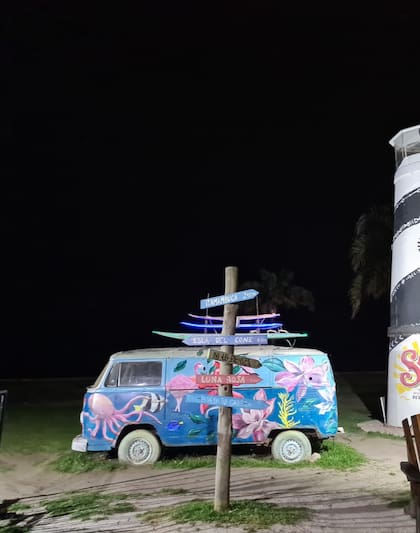 La van estilo surfer y el faro, detrás, una opción para no poner el clásico cartel con nombre del lugar, en este caso Malloys en la costa de Martínez