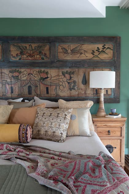 Lámpara de mesa ‘Hamilton’ de Desde Asia. Mesa de luz antigua restaurada, parte de la colección personal de Cecilia. Cabecero con panel oriental tallado sobre pared verde y textiles en dorado, crudo y terracota.