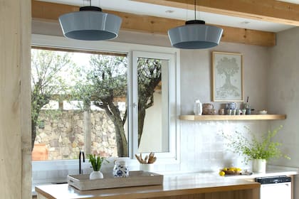 Lámparas (Tienda Cartago) de un celeste grisáceo que va muy bien con la madera de kiri, los mosaicos estilo zellige y el patio con paredes de piedra y olivos en esta cocina proyectada por Estudio Estudio.