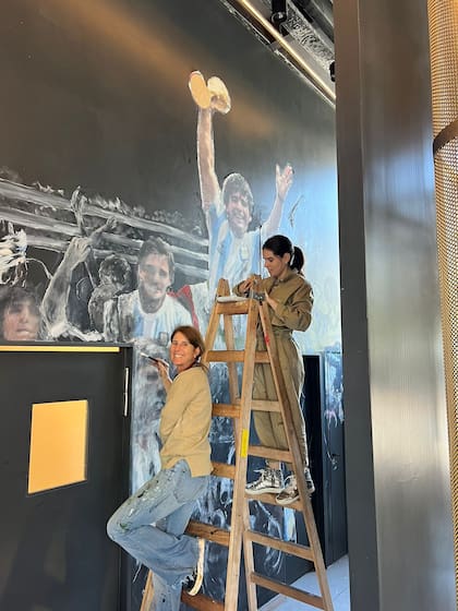 Las artistas plásticas Catalina Ruiz y Male Inurrigarro se encuentran en pleno proceso de pintar un mural de Maradona levantando la copa del mundo como en el mundial de México 1986