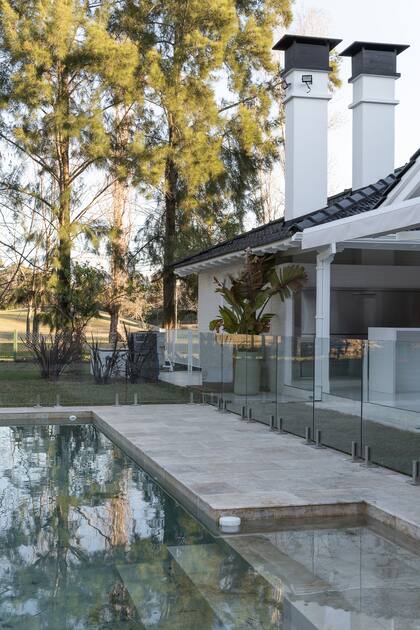 Las baldosas de mármol travertino acompañan la calidez de los materiales interiores. El cerco de vidrio permite que el jardín ingrese al quincho.