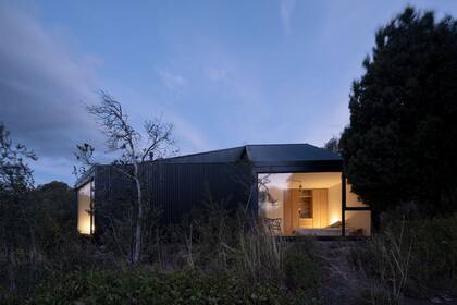 Vista nocturna del cuarto principal y la calidez de las luces indirectas. Aprovechando las pendientes se sumaron dos dormitorios pequeños con un segundo baño en planta alta.