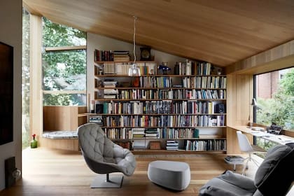 Las estanterías de madera combinan con el piso y el rincón de lectura, que tiene una vista relajante desde una ventana del piso al techo.