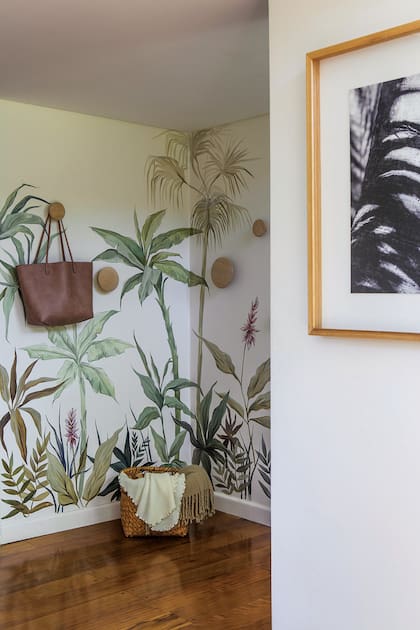 Las fotografías de Silvina (dueña de casa) se llevan a la perfección con el mural botánico de Florencia Chedufau, que le dio vida a este lugar de paso. Cuando la casa se llena de invitados, los percheros redondos (Broca Muebles) suman función al paisaje tropical.