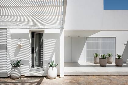Las paredes, las puertas de hierro y el varillado de aluminio que cubre el ventanal están pintados de blanco, el color que le da identidad a la casa. El piso es de cemento alisado gris perla. Aberturas (Marroncelli). En macetas del mismo tono que el piso, los cuatro agaves dan el único toque de color.