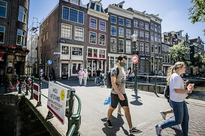 Las personas, con una máscara facial, caminan por un puente del barrio rojo, en Amsterdam