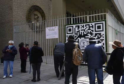 Las personas miran un código QR afuera del Banco Central de Bolivia que las personas deben usar para registrarse para hacer una cita con el banco que luego le dice al usuario cuántos dólares estadounidenses puede comprar en esa fecha