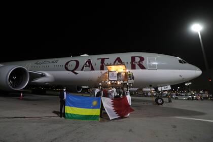 Las personas sostienen las banderas de Ruanda y Qatar frente a un vuelo de Qatar Airways que llevará suministros médicos a Kigali donados por el Fondo de Qatar para el Desarrollo