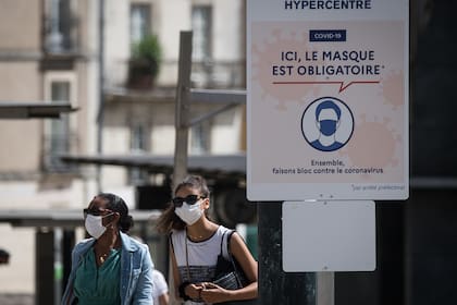 Las personas usan máscaras protectoras mientras pasean por una calle junto a un letrero que dice "Aquí la máscara es obligatoria" en Nantes, en el oeste de Francia, el 21 de agosto de 2020