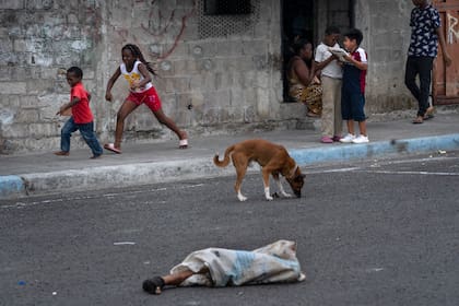 Las piernas de un hombre desmembrado sobresalen de una bolsa en la calle donde juegan niños y deambulan perros en el barrio Colinas de La Florida en Guayaquil, Ecuado (Foto AP/Rodrigo Abd)