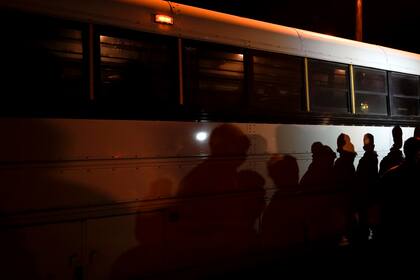 Las sombras de los migrantes alineados se proyectan a lo largo de un autobús, después de entregarse al cruzar la frontera entre Estados Unidos y México en Roma, Texas