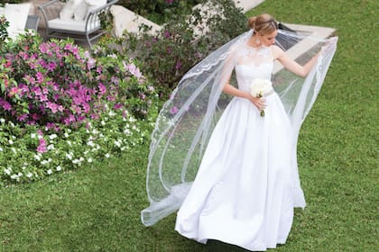 Laurencio Adot creó este diseño con falda tableada, en seda natural y tul bordado. La cintura con strass y cristales de plata. El velo, en tul de ilusión, con guarda de hilos de plata.