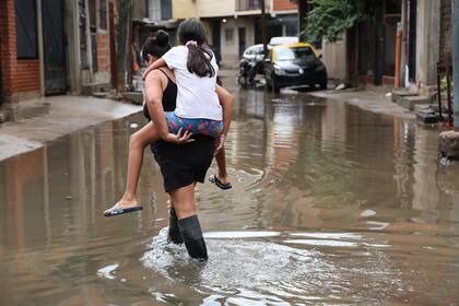  Lazo junto a su hija Nayla, cruzando una calle inundada en el barrio Radio Estación