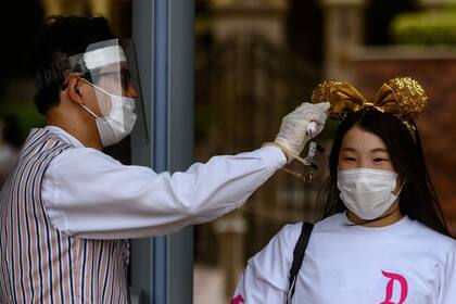 Le toman la temperatura a una niña con mascarilla en Disneyland Tokyo