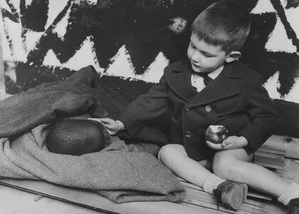 Leyenda original: "Un niño negro cerca de sus padres, artesanos indígenas que ejercen su oficio frente a las cabañas construidas para ellos en los jardines tropicales, toma una siesta en la "barza". Un niño blanco encuentra a su hermanito negro tan amable".
Foto: Rmca Tervuren