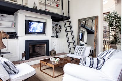 Living con mesa baja de lapacho (La Viruta), sillones con fundas de lino, almohadones rayados (De Levie) y gran espejo con marco decapado (Los Díaz de Mario).