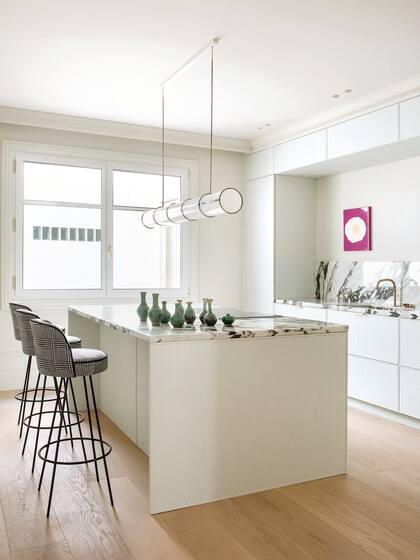Lo diáfano de la cocina realza las líneas de mesadas y alzada, la lámpara tubular y el tapizado en pied-de-poule de las banquetas.