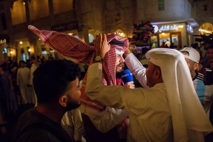 Locales le colocan un ghutra a un periodista en el Souq Waqif de Doha, Qatar. (Tasneem Alsultan/The New York Times)