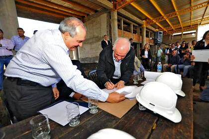 López sostiene una de las hojas mientras Morelli firma el convenio en medio de la terminal en construcción