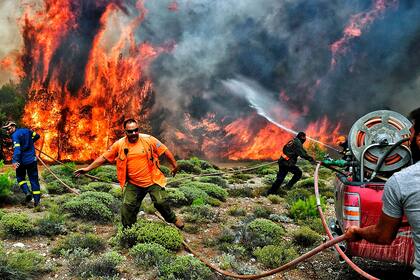 Los bomberos y voluntarios intentan extinguir las llamas durante un incendio forestal en la aldea de Kineta, cerca de Atenas