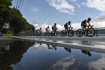 Los ciclistas del pelotón se reflejan en un charco mientras pasan por el lago Yamanaka durante la carrera ciclista en ruta masculina de los Juegos Olímpicos de Tokio 2020 en la prefectura de Yamanashi, Japón, el 24 de julio de 2021.