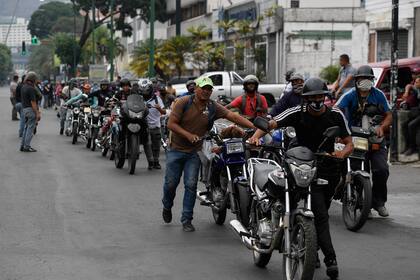 Los ciclistas empujan sus motocicletas en una fila para repostar sus tanques en una estación de servicio, en Caracas, el 25 de mayo de 2020, en medio del brote de coronavirus