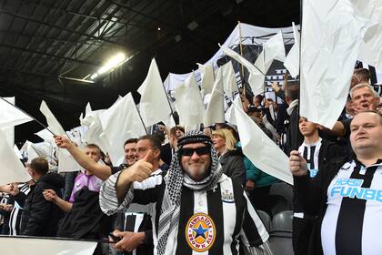 Los fanáticos del Newcastle United ondean banderas y pancartas en blanco y negro que celebran la reciente toma de posesión del club por parte de un consorcio liderado por Arabia Saudita. El último dueño, Mike Ashley, se fue repudiado luego de 14 años de gestión