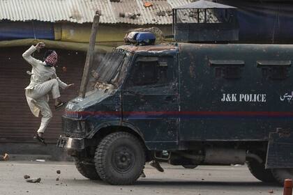 Un manifestante enmascarado de Cachemira salta al capó de un vehículo blindado de la policía de la india mientras le arroja piedras durante una protesta en Srinagar, Cachemira