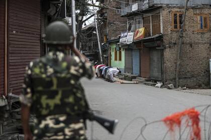 Un soldado paramilitar indio está de guardia mientras los musulmanes de Cachemira ofrecen las oraciones de los viernes en una calle frente a una mezquita local durante el toque de queda como restricciones en Srinagar