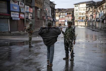 Un soldado paramilitar indio le ordena a un cachemir abrir su chaqueta antes de registrarlo durante el toque de queda en Srinagar