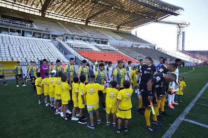 Los futbolistas se preparan para ingresar, los chicos los rodean y los saludan; de fondo, la platea del estadio Mundialista en la que no puede ingresar el público