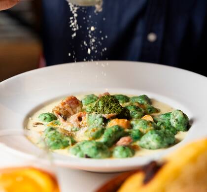 Los gnocchi soufflé de espinaca gratinados con ave, crema, champignon, pesto, jamón cocido y parmesano de La Parolaccia