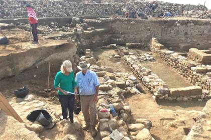 Los investigadores se paran cerca de las ruinas de muros antiguos, con la capa de destrucción a la mitad de cada muro expuesto