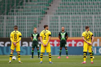 Los jugadores de Dortmund, primer plano y Wolfsburg permanecen en el campo durante un minuto de silencio por las víctimas de COVID-19 antes del partido de fútbol de la Bundesliga alemana entre el VfL Wolfsburg y el Borussia Dortmund en Wolfsburg, Alemania.