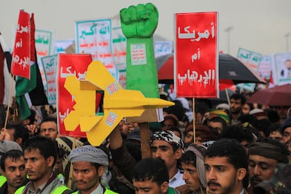 Los manifestantes levantan un puño simulado y un avión de combate, y carteles en árabe que dicen "Estados Unidos es la madre del terrorismo" durante una manifestación antiisraelí y antiestadounidense en Saná, la capital controlada por los hutíes, el 19 de enero de 2024, en protesta contra Estados Unidos.