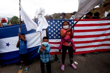 Los migrantes hondureños izan banderas blancas frente a una bandera hondureña y a una estadounidense, mientras los soldados y la policía guatemaltecos les impiden avanzar hacia la frontera con Estados Unidos