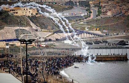 Mientras el ejército realiza fogoneos disuasivos, los migrantes marroquíes se escabullen a través de una valla en la ciudad norteña de Fnideq en un intento de cruzar la frontera de Marruecos al enclave español de Ceuta en el norte de África el 18 de mayo de 2021