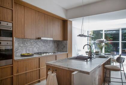 Los muebles enchapados fueron diseñados por el estudio, igual que la lámpara de chapa plegada y cromada. Las banquetas son el modelo 42 de La Feliz.