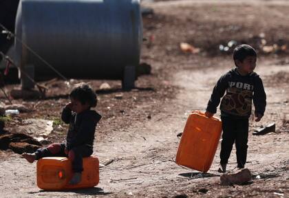 Los niños cargan bidones en un campamento de desplazados internos en el noroeste de Siria